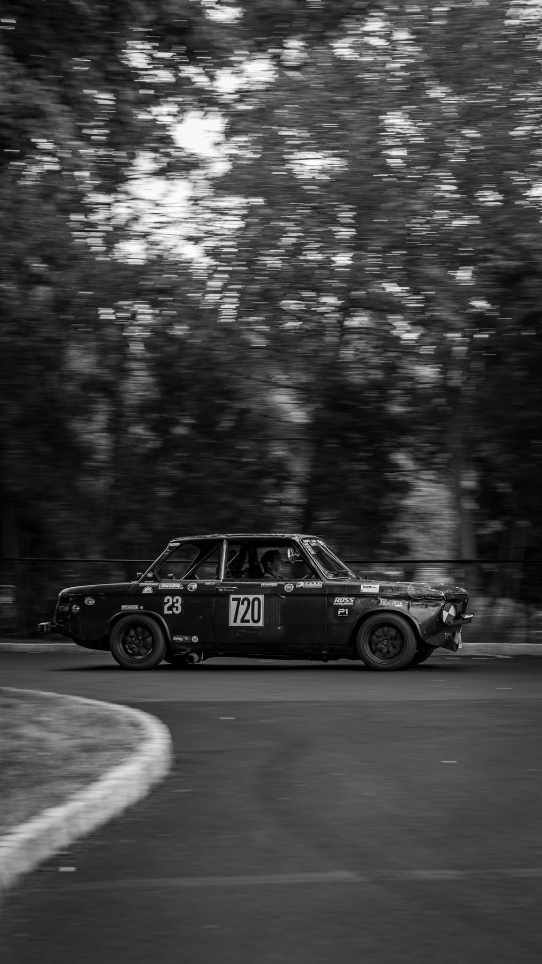 Black and white shot of a vintage BMW 2002 race car at speed
