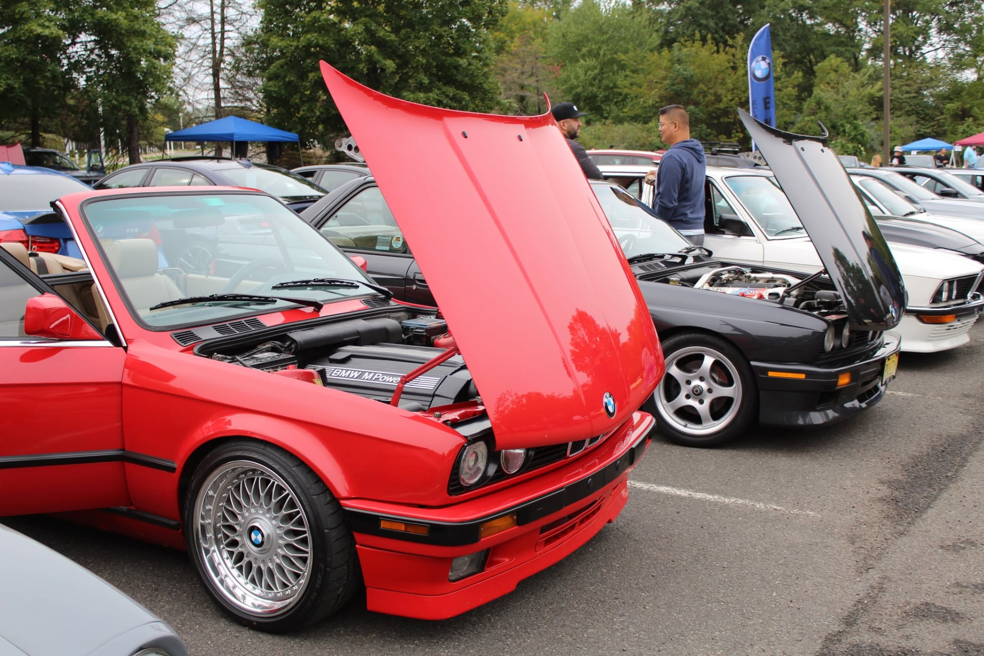 Red BMW E30 convertible with its hood up beside other E30s