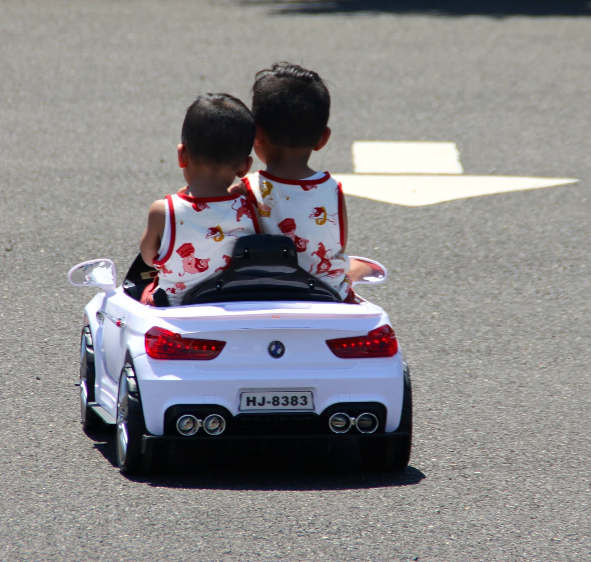 Two kids driving a mini BMW ride-on car across the show lot